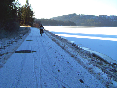 Cyclist on Trail of the Coeur d'Alenes with snow on trail and lake